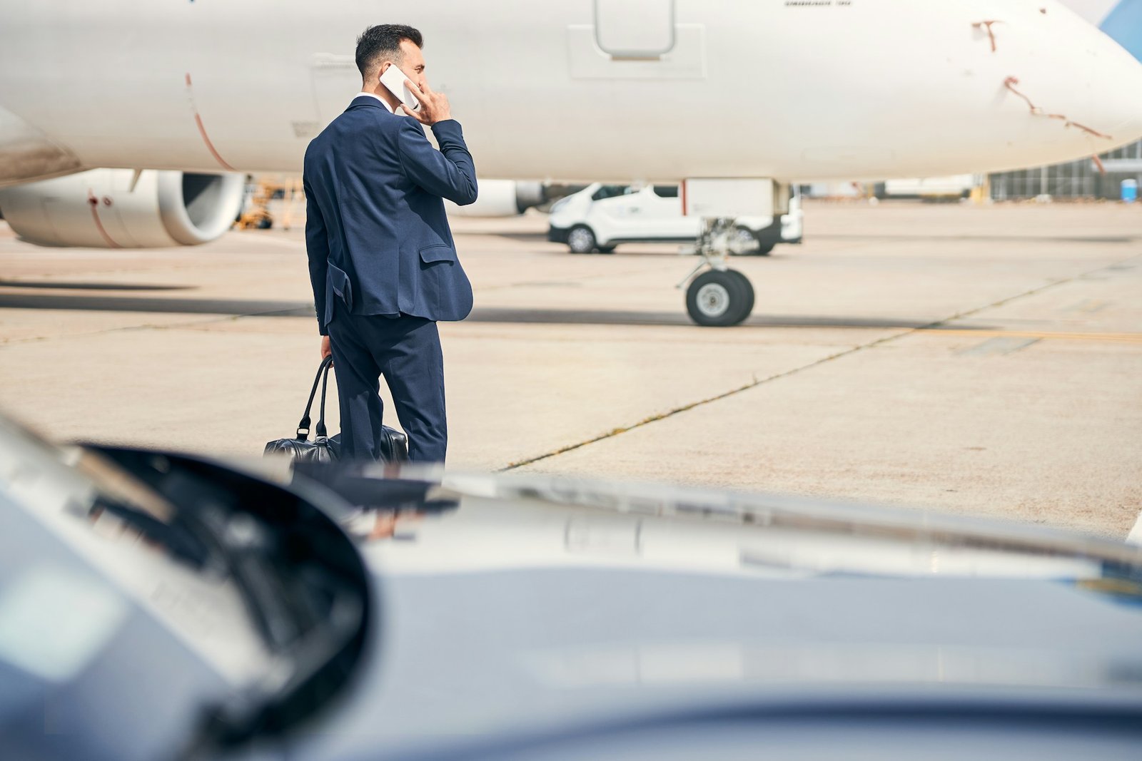 Business traveler on tarmac near private jet using phone, awaiting private car service